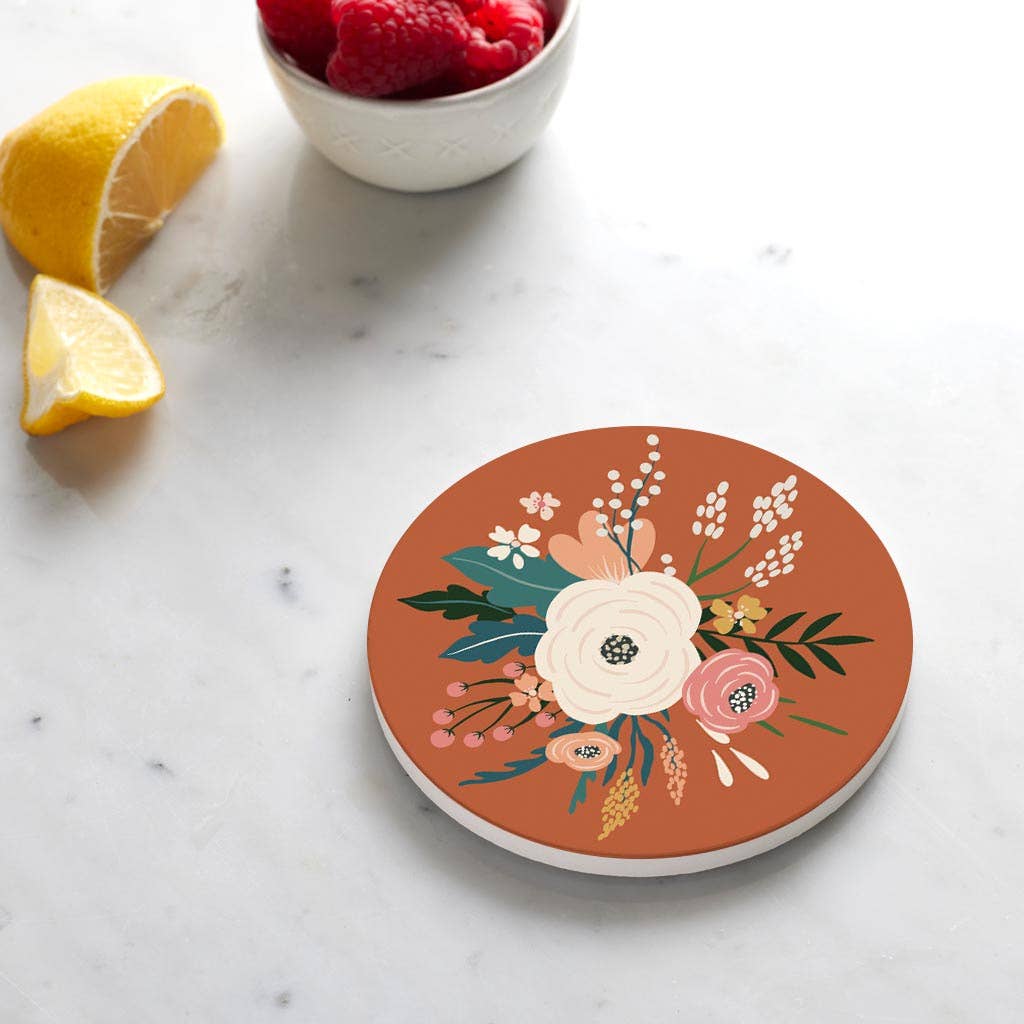 A round coaster with a terracotta background and a colorful floral illustration.