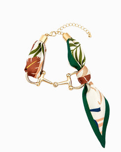 A gold-tone horsebit chain bracelet featuring two decorative end pieces made from a printed silk scarf with green, brown, and cream tropical leaf patterns, shown on a plain white background.